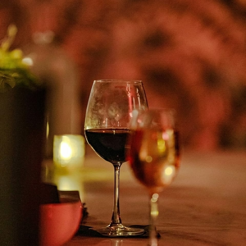 Two wine glasses, one with red wine, on a bar with warm lighting and blurred background.