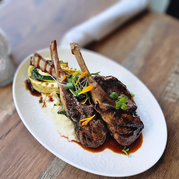 Grilled lamb chops with mashed potatoes, zucchini, and a rich brown sauce on a white plate.
