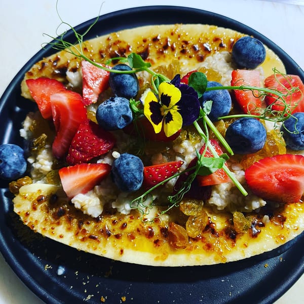 Banana split with oatmeal, blueberries, strawberries, golden raisins, and edible flowers.