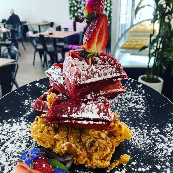 Red velvet waffles and fried chicken, dusted with powdered sugar and garnished with strawberries.