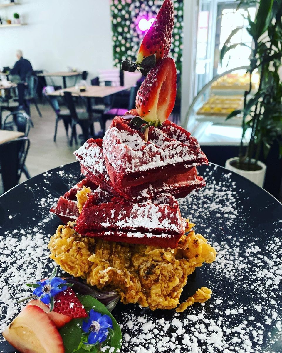 Red velvet waffles and fried chicken, dusted with powdered sugar and garnished with strawberries.