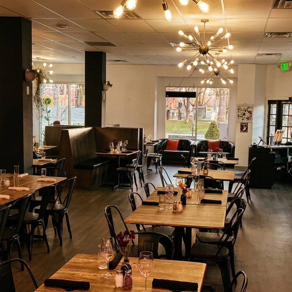 Spacious, modern restaurant interior with wooden tables, black chairs, booth seating, and decorative light fixtures.