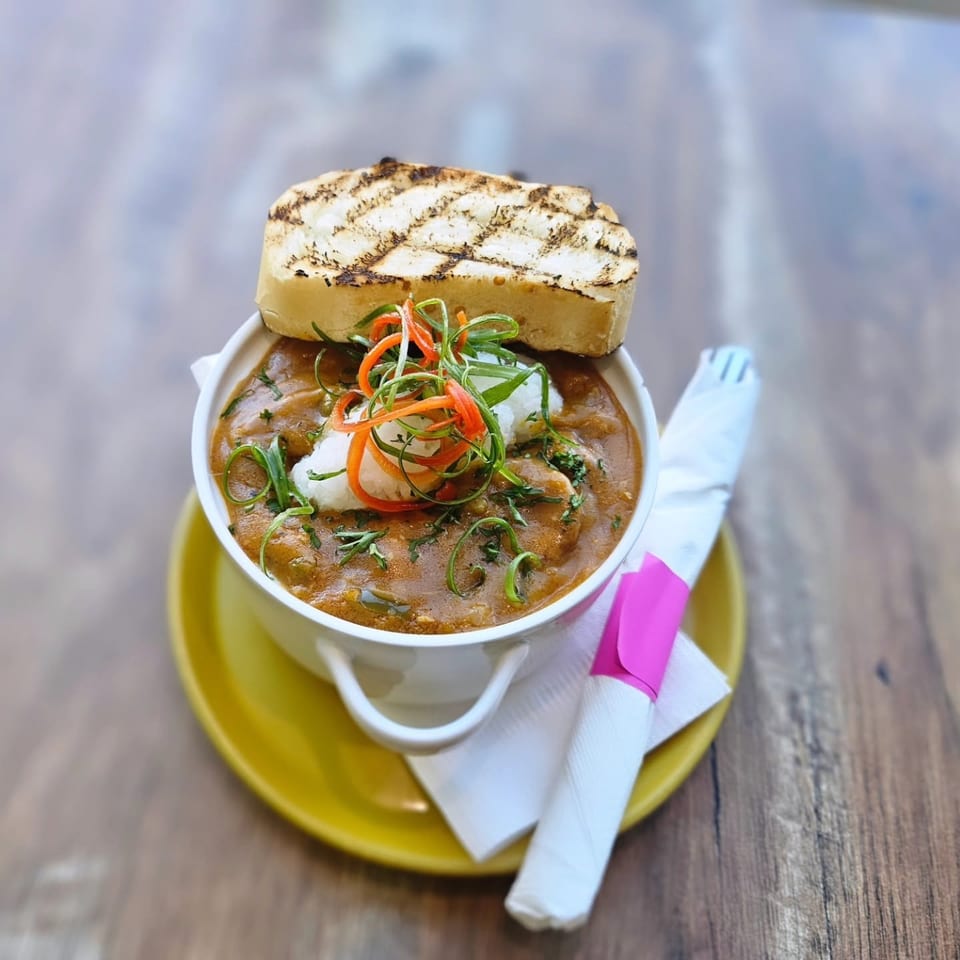 Hearty stew in a white bowl with grilled bread, garnished with fresh herbs and vegetables.